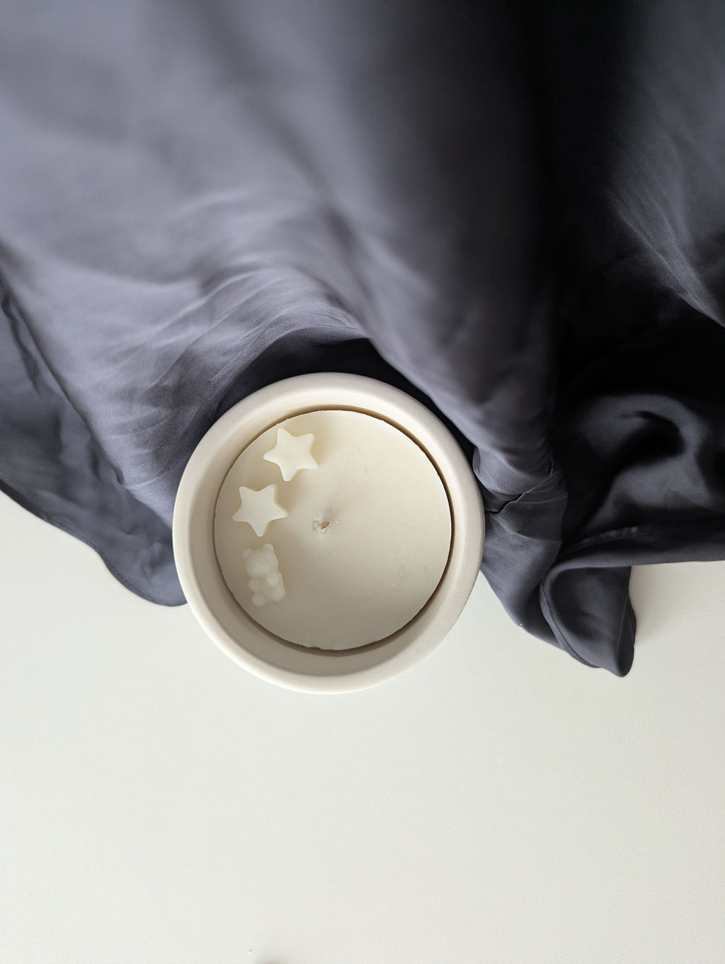 Bougie artisanale parfumée vue du dessus avec cire délicate et composition pour annonce grossesse, naissance, bébé montrant deux étoiles et un nounours.
