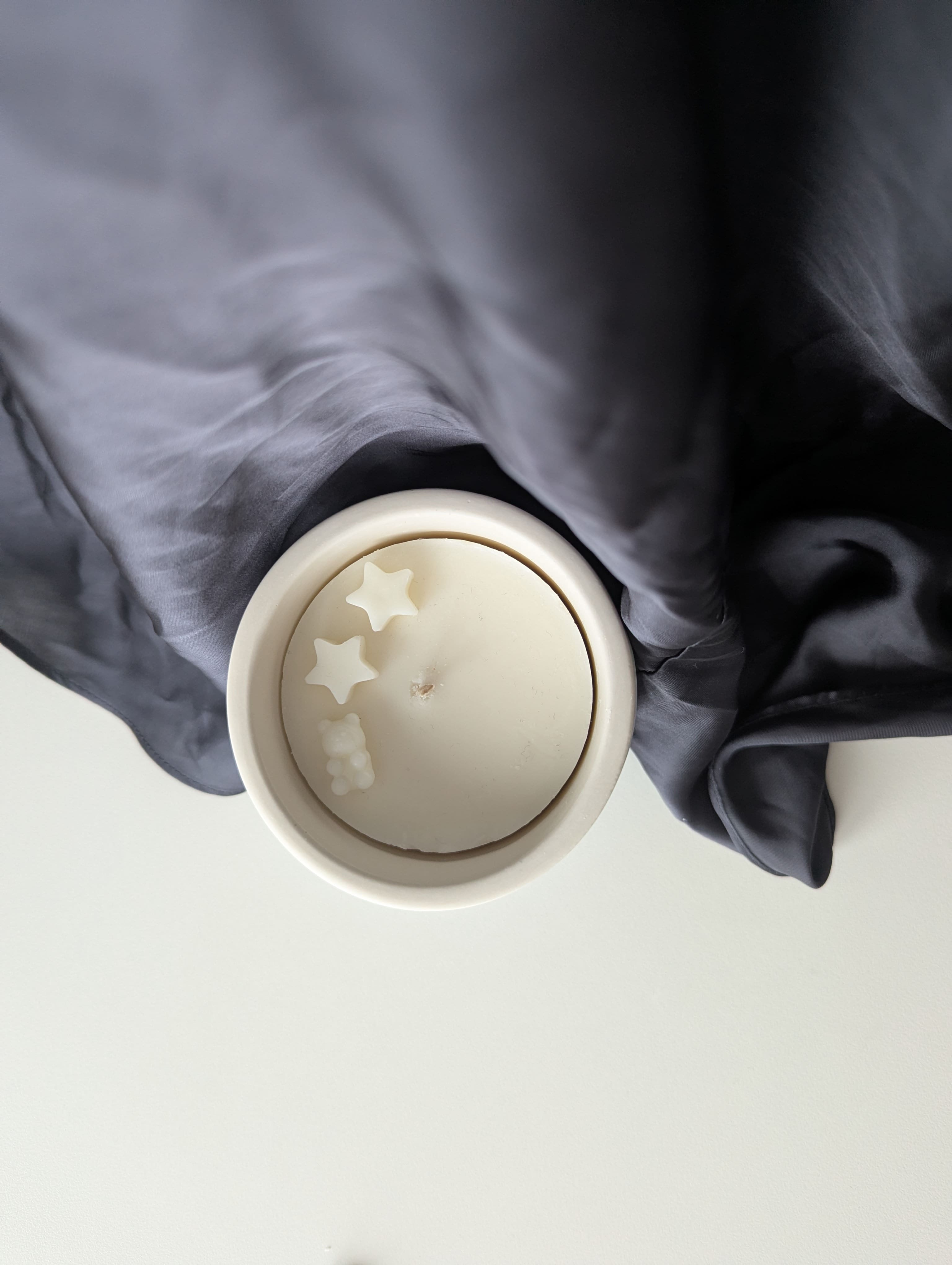 Bougie artisanale parfumée vue du dessus avec cire délicate et composition pour annonce grossesse, naissance, bébé montrant deux étoiles et un nounours.
