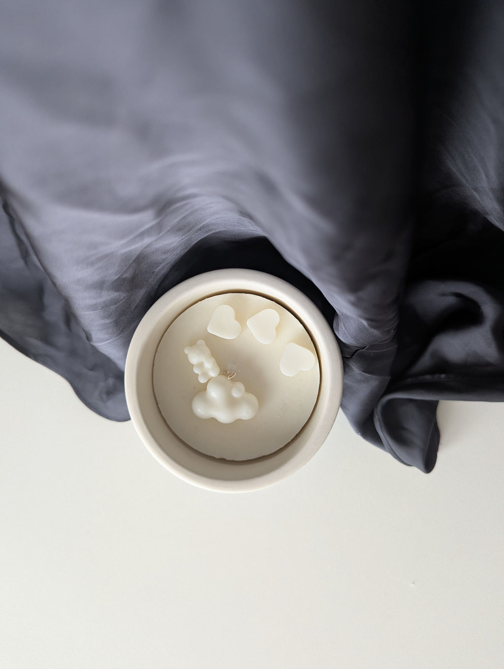 Bougie artisanale parfumée vue du dessus avec cire délicate et composition pour annonce grossesse, naissance, bébé montrant trois cœurs, un nounours et un nuage.